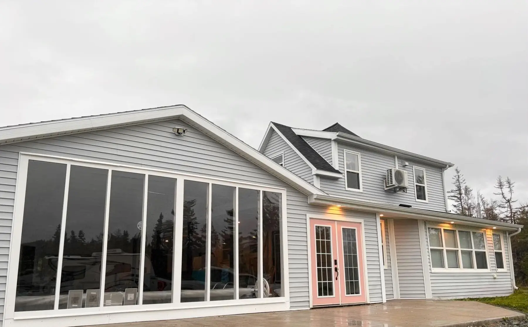 The Old Farmhouse from outside: grey siding, pink French doors and the glass-walled pool room